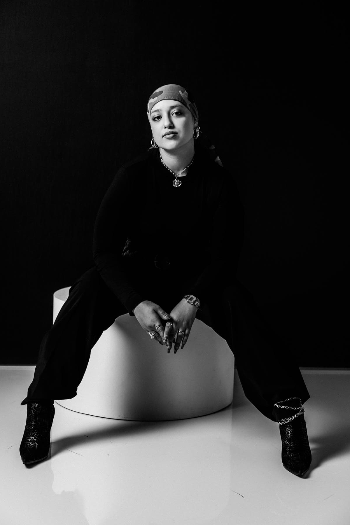 Seated editorial portrait in black with a printed headwrap, black and white